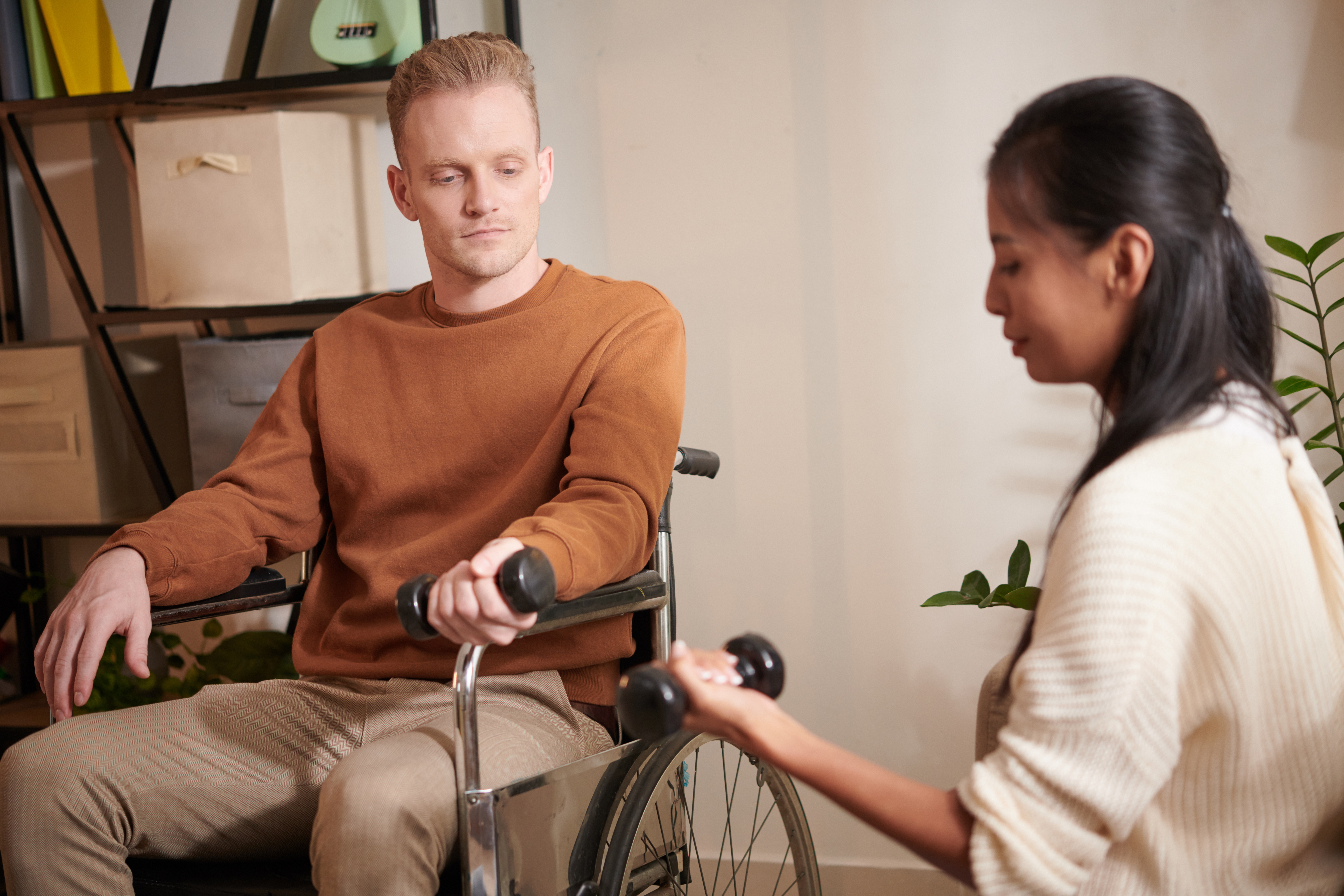 Jeune soignante montrant à un homme handicapé comment faire de l'exercice avec des haltères